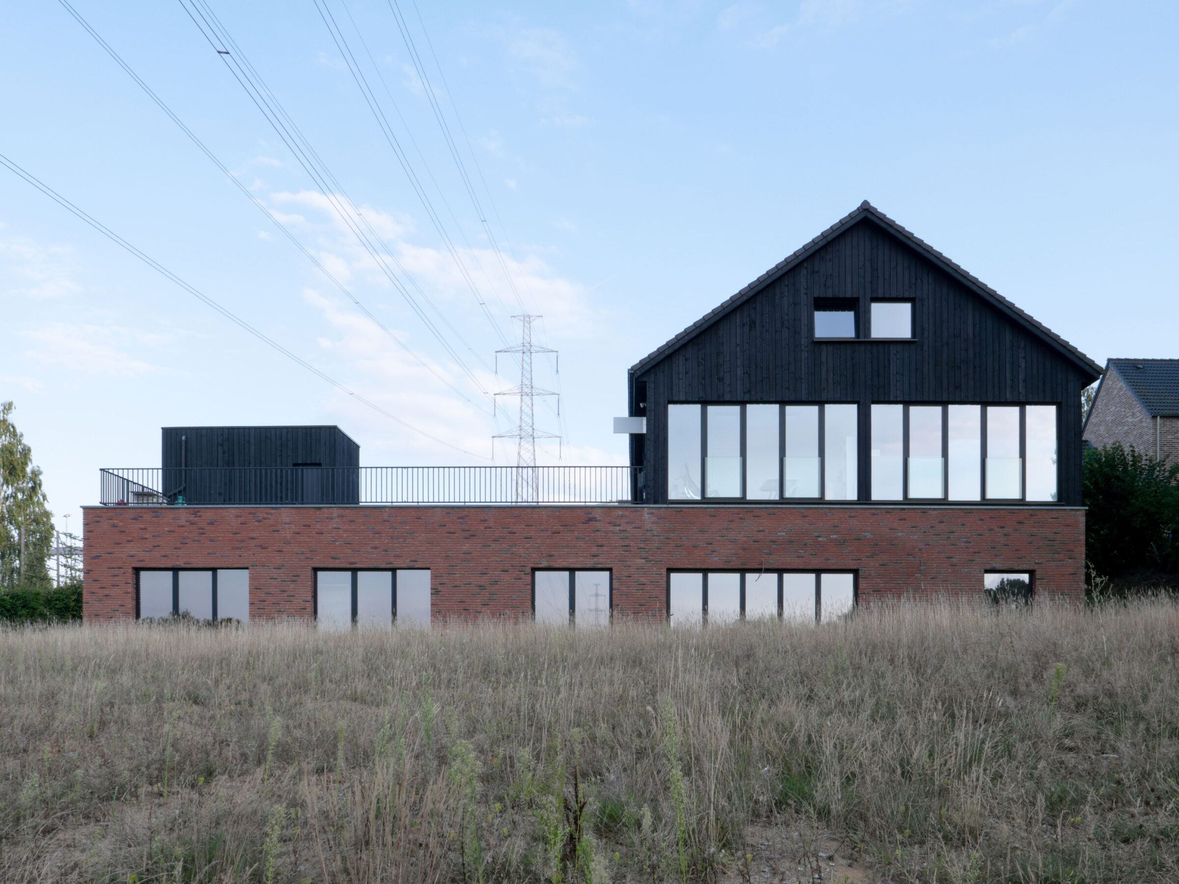 Vue dans le paysage rural d'une pharmacie et maison médicale à Ittre réalisé par fp-architectes. Matériaux en bois brûlé et briques de terre cuite.